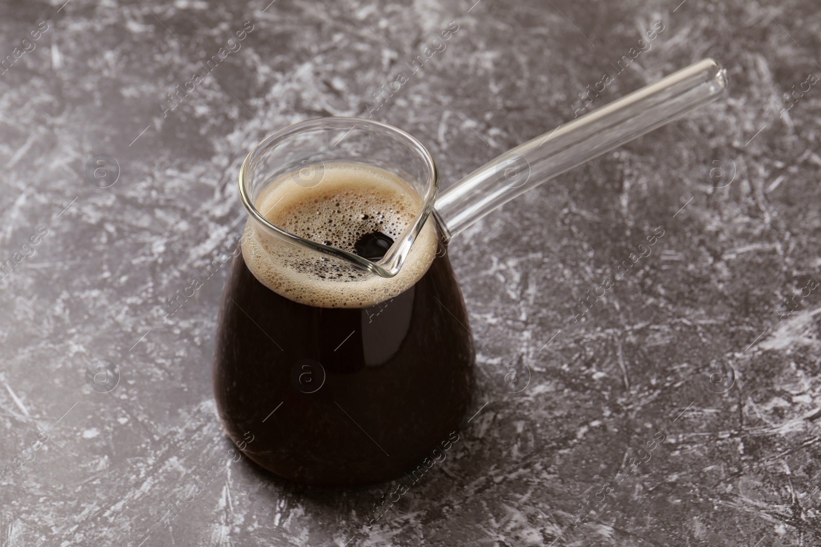 Photo of Turkish coffee in glass cezve on grey marble table