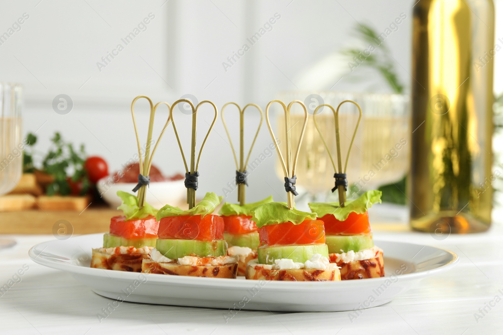 Photo of Tasty canapes with salmon, cucumber, bread and cream cheese on white wooden table, closeup