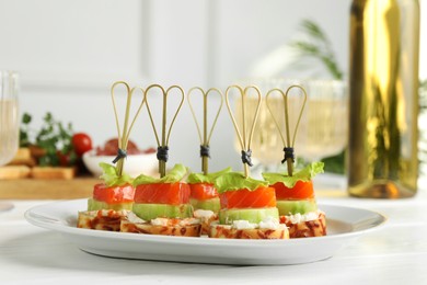 Photo of Tasty canapes with salmon, cucumber, bread and cream cheese on white wooden table, closeup