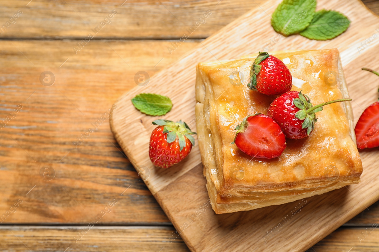 Photo of Fresh delicious puff pastry with sweet strawberries on wooden table, top view. Space for text