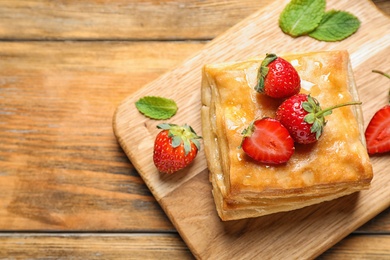 Fresh delicious puff pastry with sweet strawberries on wooden table, top view. Space for text