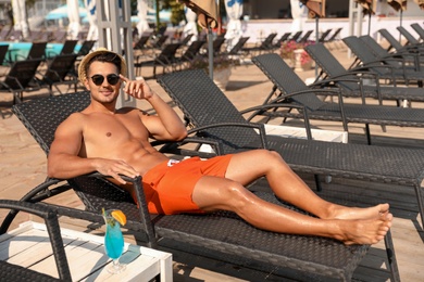 Photo of Young man with cocktail on lounge chair near outdoor pool