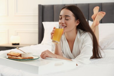 Photo of Happy young woman having breakfast on bed at home