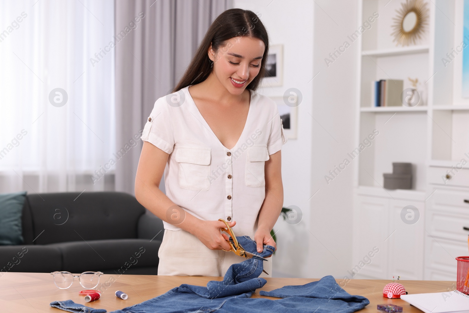 Photo of Happy woman cutting hem of jeans at table indoors