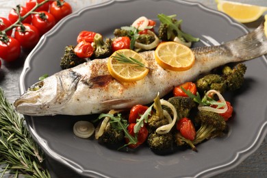 Photo of Baked fish with vegetables, rosemary and lemon on grey wooden table, closeup