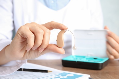 Photo of Doctor holding hearing aid at table, closeup. Medical device