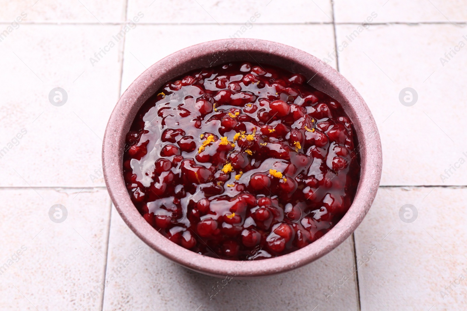 Photo of Tasty cranberry sauce in bowl on white tiled table