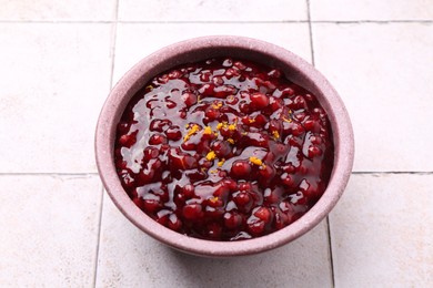 Tasty cranberry sauce in bowl on white tiled table