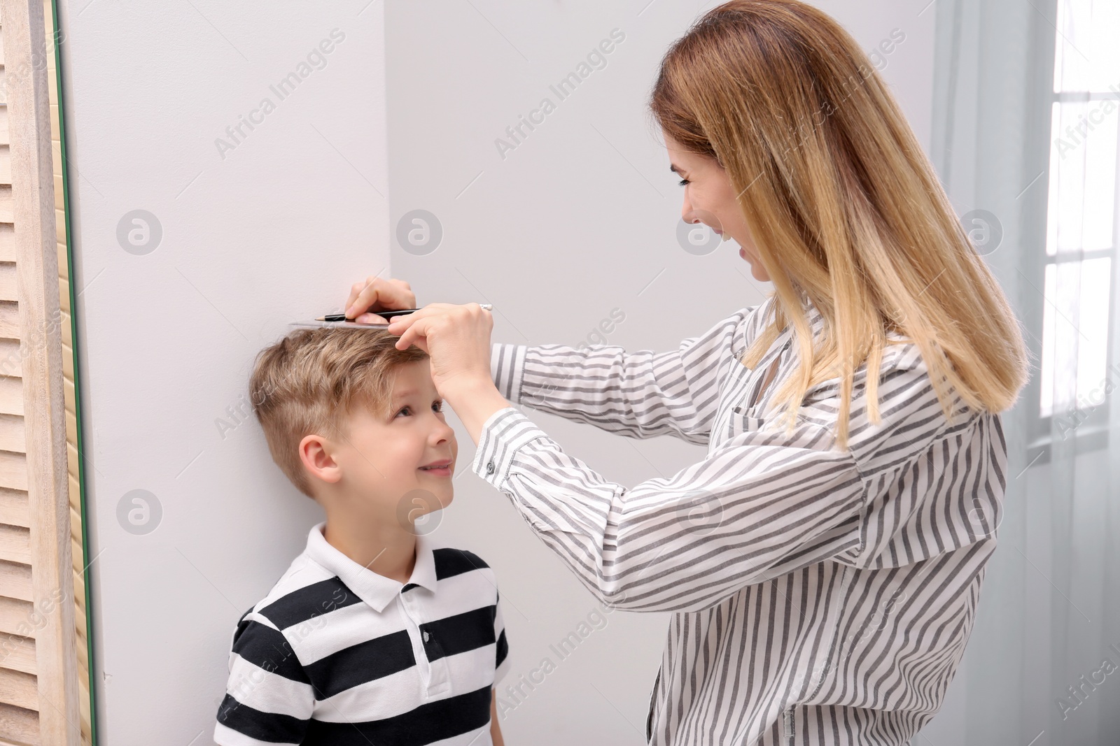 Photo of Young woman measuring her son's height at home