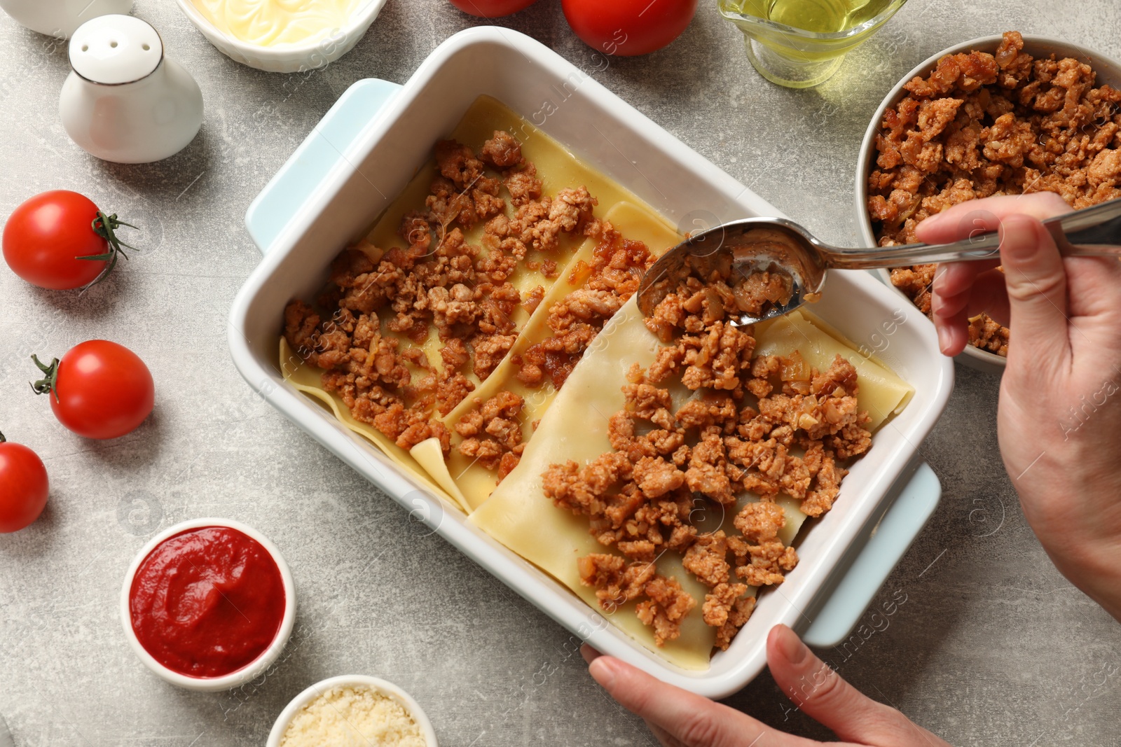 Photo of Woman making lasagna at light grey textured table, top view