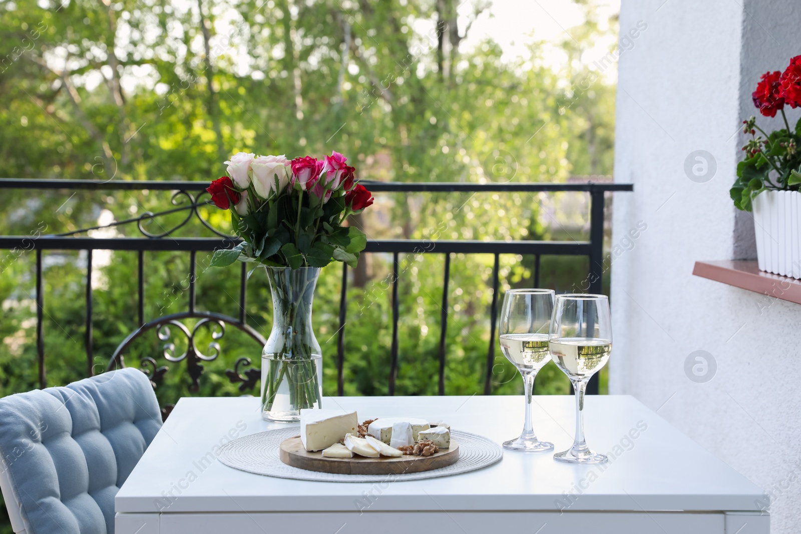 Photo of Beautiful roses, glasses of wine and snacks on white table at balcony