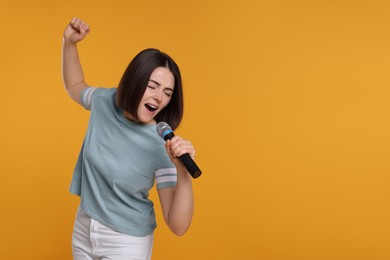 Photo of Beautiful young woman with microphone singing on yellow background, space for text