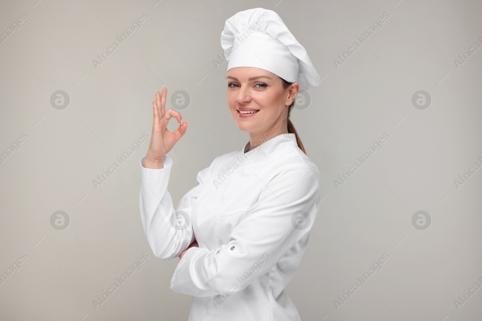 Photo of Happy chef in uniform showing OK gesture on grey background