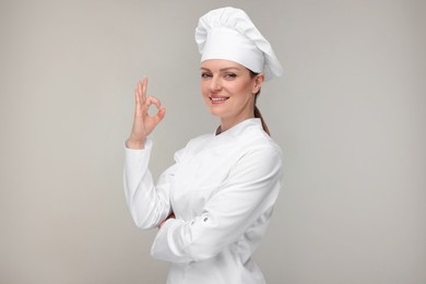 Happy chef in uniform showing OK gesture on grey background