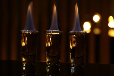 Flaming alcohol drink in shot glasses on mirror surface against blurred background