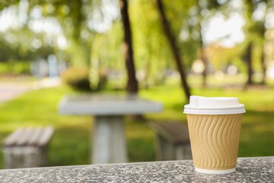 Photo of Paper cup on parapet in park, space for text. Coffee to go