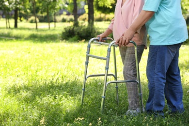 Elderly man helping his wife with walking frame outdoors, closeup