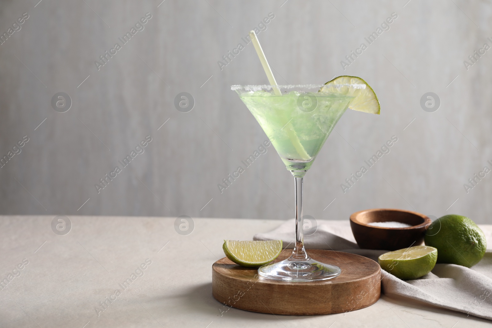 Photo of Delicious Margarita cocktail in glass, salt and limes on light table, space for text