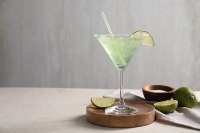 Delicious Margarita cocktail in glass, salt and limes on light table, space for text