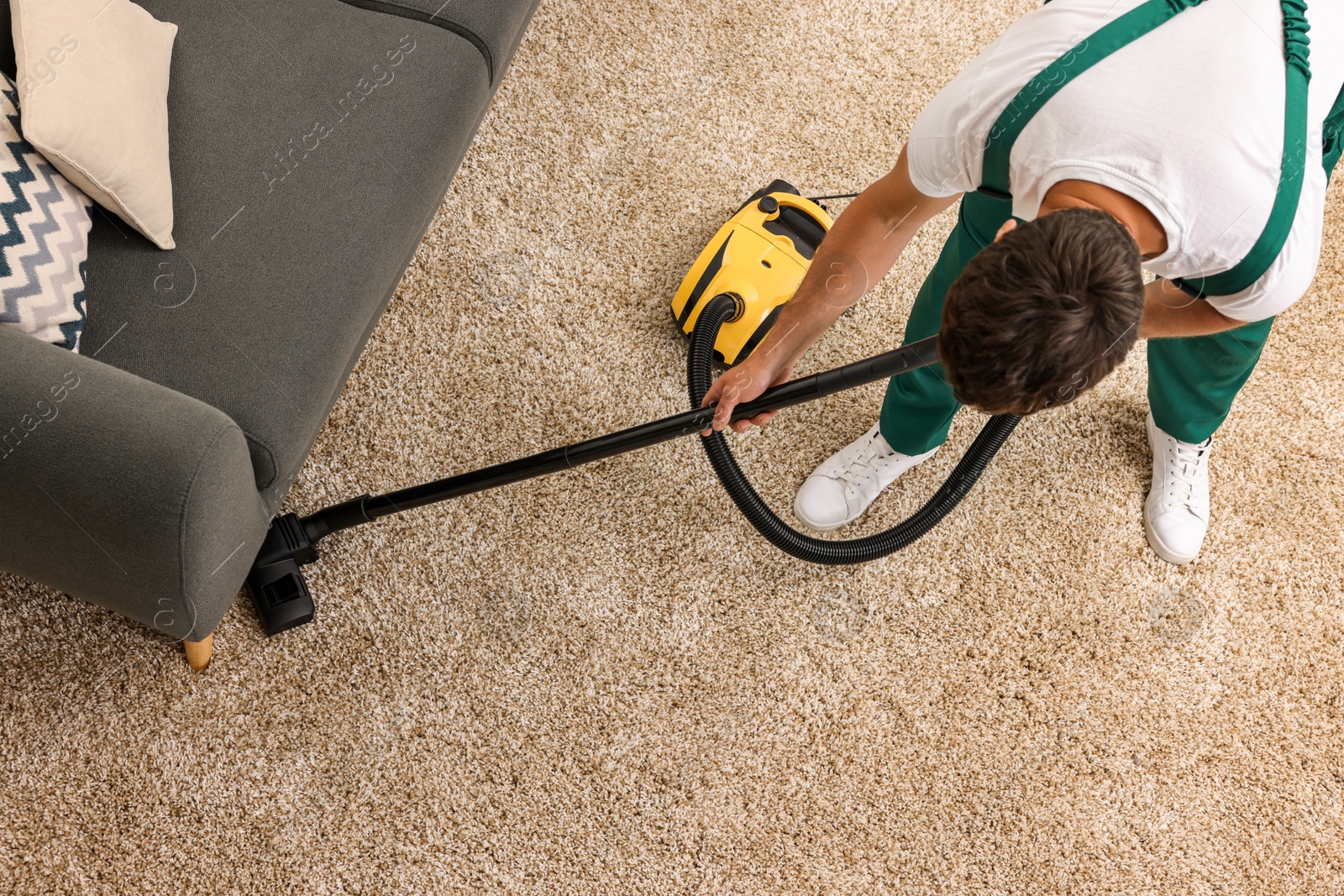 Photo of Dry cleaner's employee hoovering carpet with vacuum cleaner indoors, above view