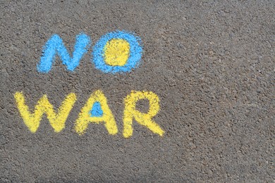 Photo of Words No War written with blue and yellow chalks on asphalt outdoors, top view. Space for text