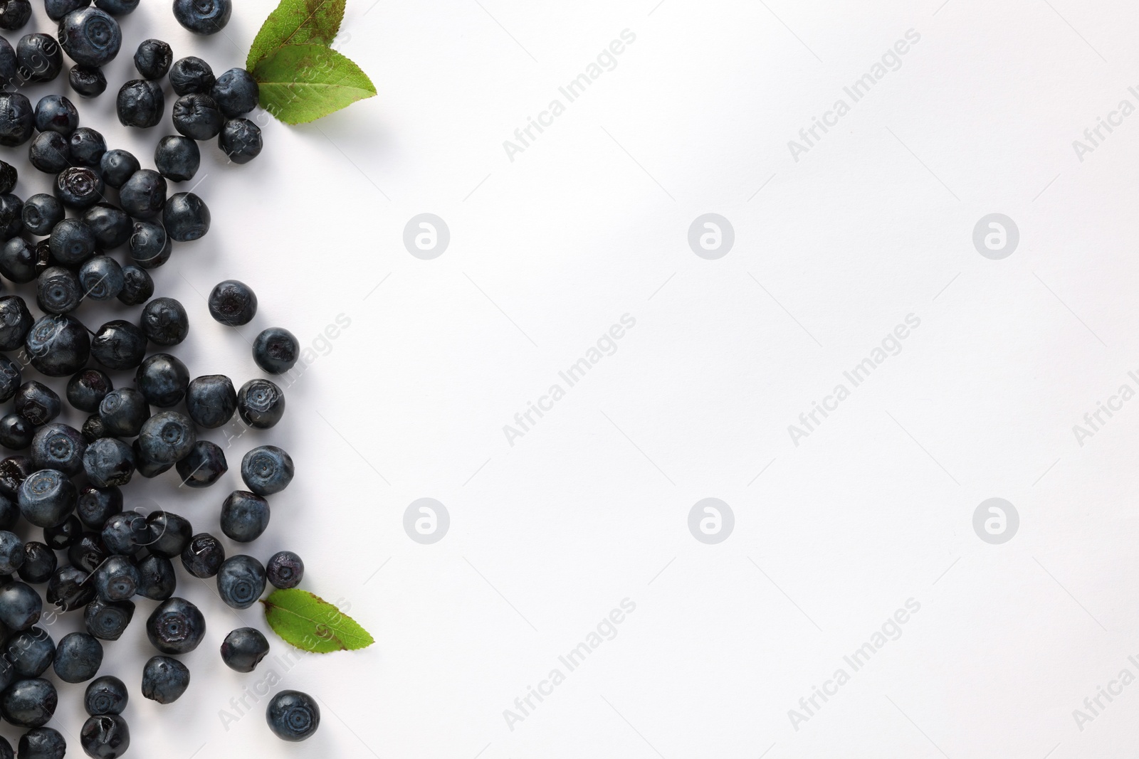 Photo of Ripe bilberries and leaves on white background, flat lay. Space for text