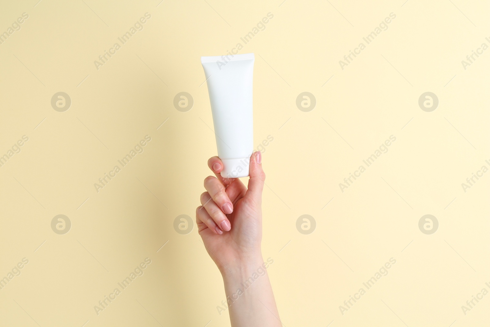 Photo of Woman holding tube of cream on yellow background, closeup