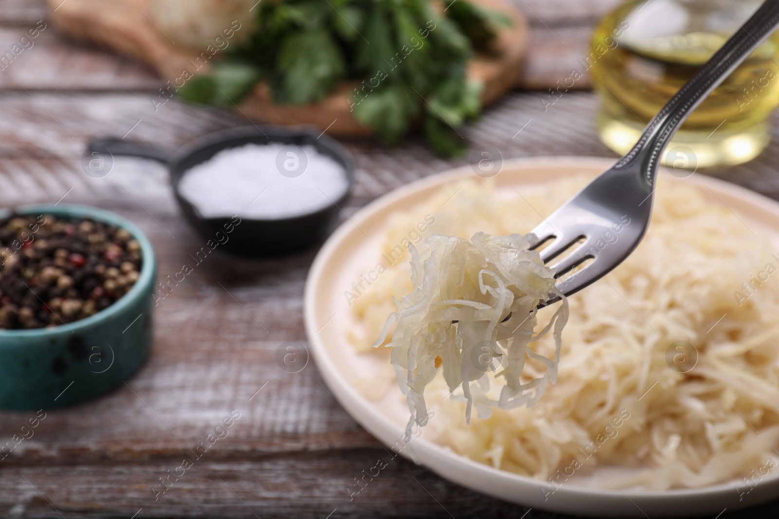 Photo of Fork with tasty sauerkraut above plate on wooden table, closeup