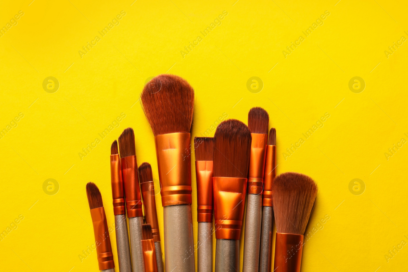 Photo of Different makeup brushes on yellow background, flat lay. Space for text