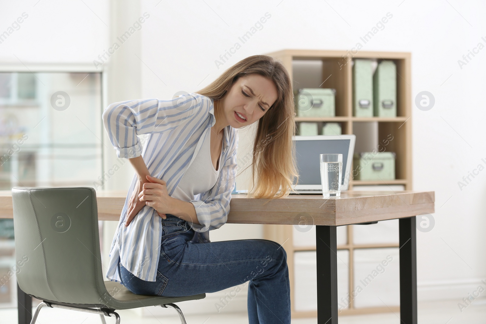 Photo of Woman suffering from back pain in office. Symptom of bad posture