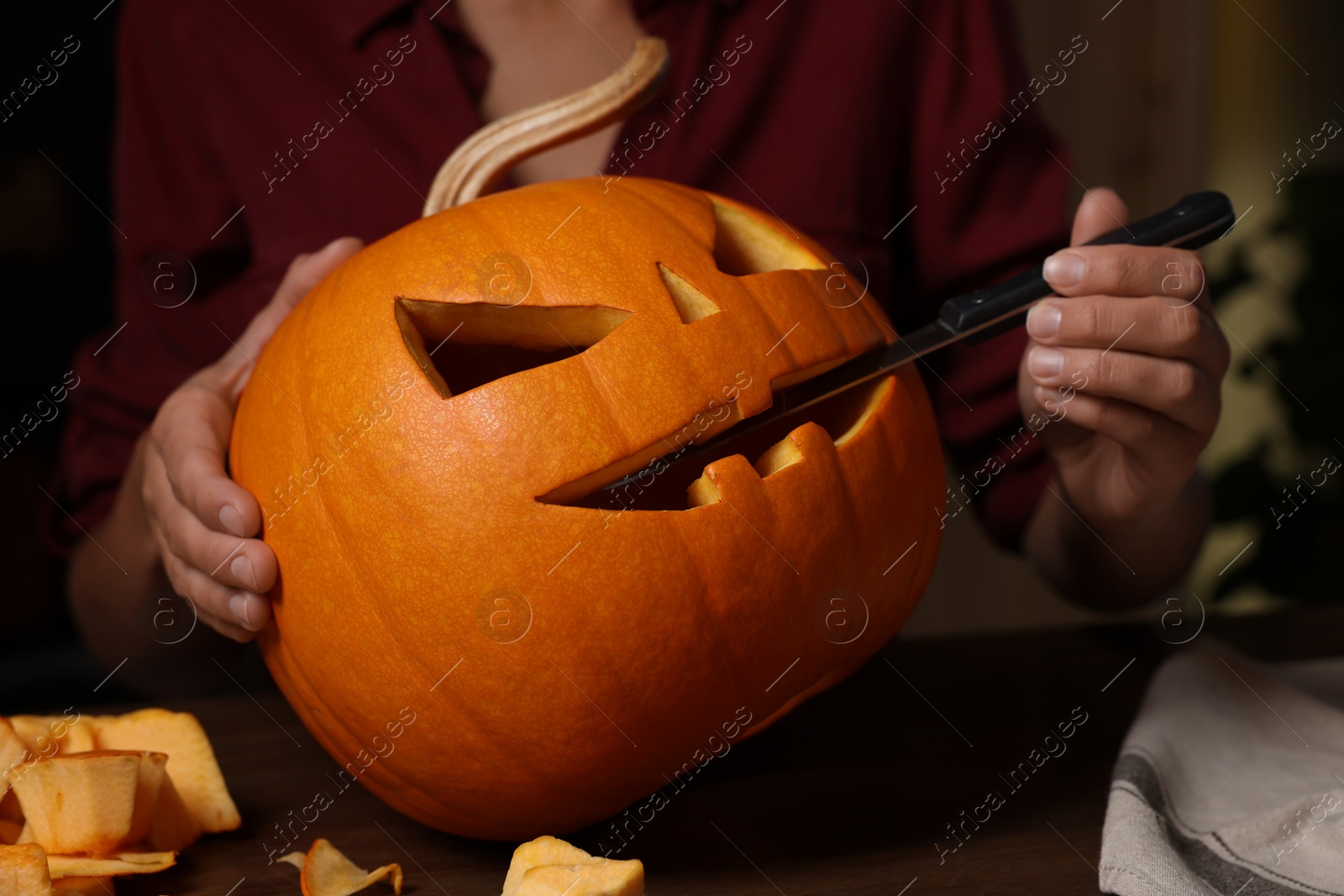 Photo of Woman carving pumpkin for Halloween at wooden table, closeup