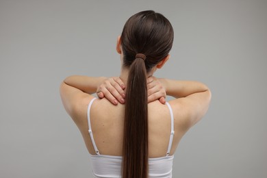 Woman touching her neck on grey background, back view