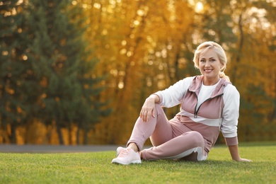 Photo of Happy mature woman sitting on grass in park