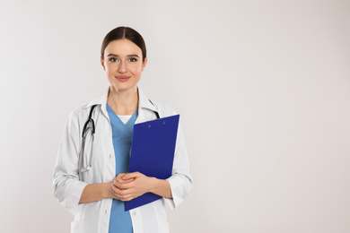 Doctor with stethoscope and clipboard on light grey background. Space for text