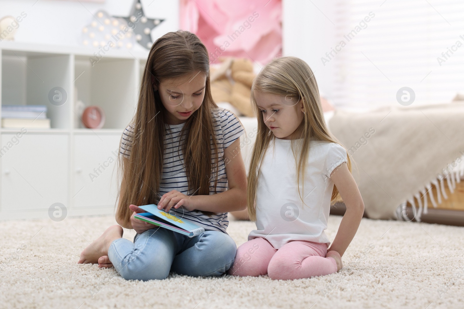 Photo of Cute little sisters reading book together at home