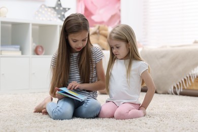 Cute little sisters reading book together at home