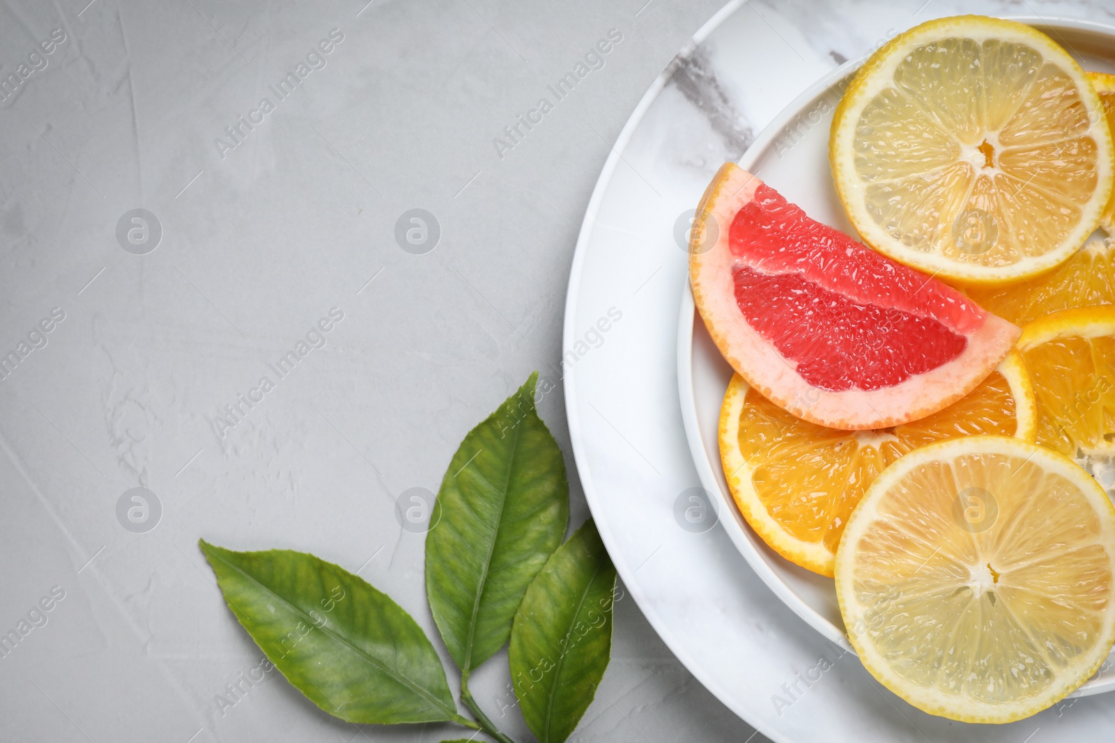 Photo of Cut citrus fruits and leaves on grey background, flat lay. Space for text