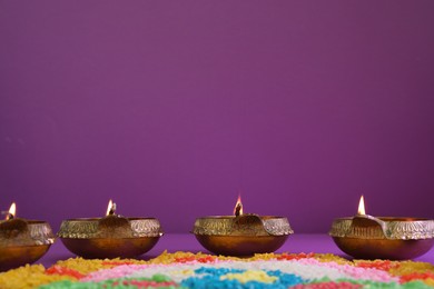 Photo of Diwali celebration. Diya lamps and colorful rangoli on purple background, space for text