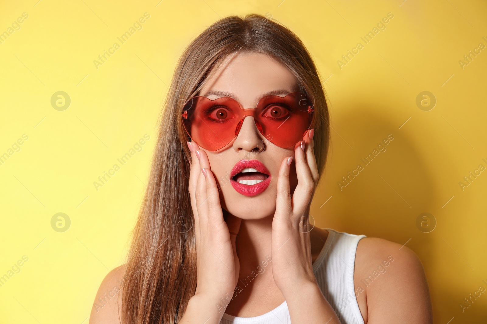 Photo of Young woman wearing stylish heart shaped sunglasses on yellow background