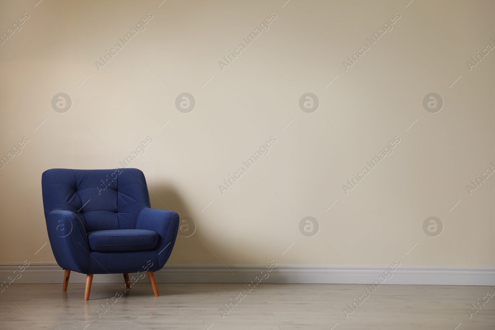 Photo of Stylish comfortable armchair near light wall in empty room. Space for text