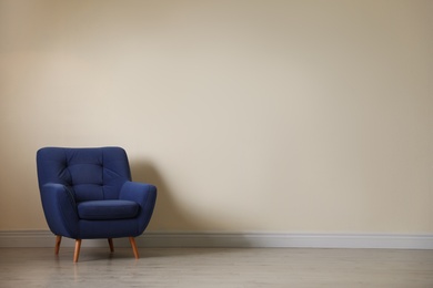 Stylish comfortable armchair near light wall in empty room. Space for text