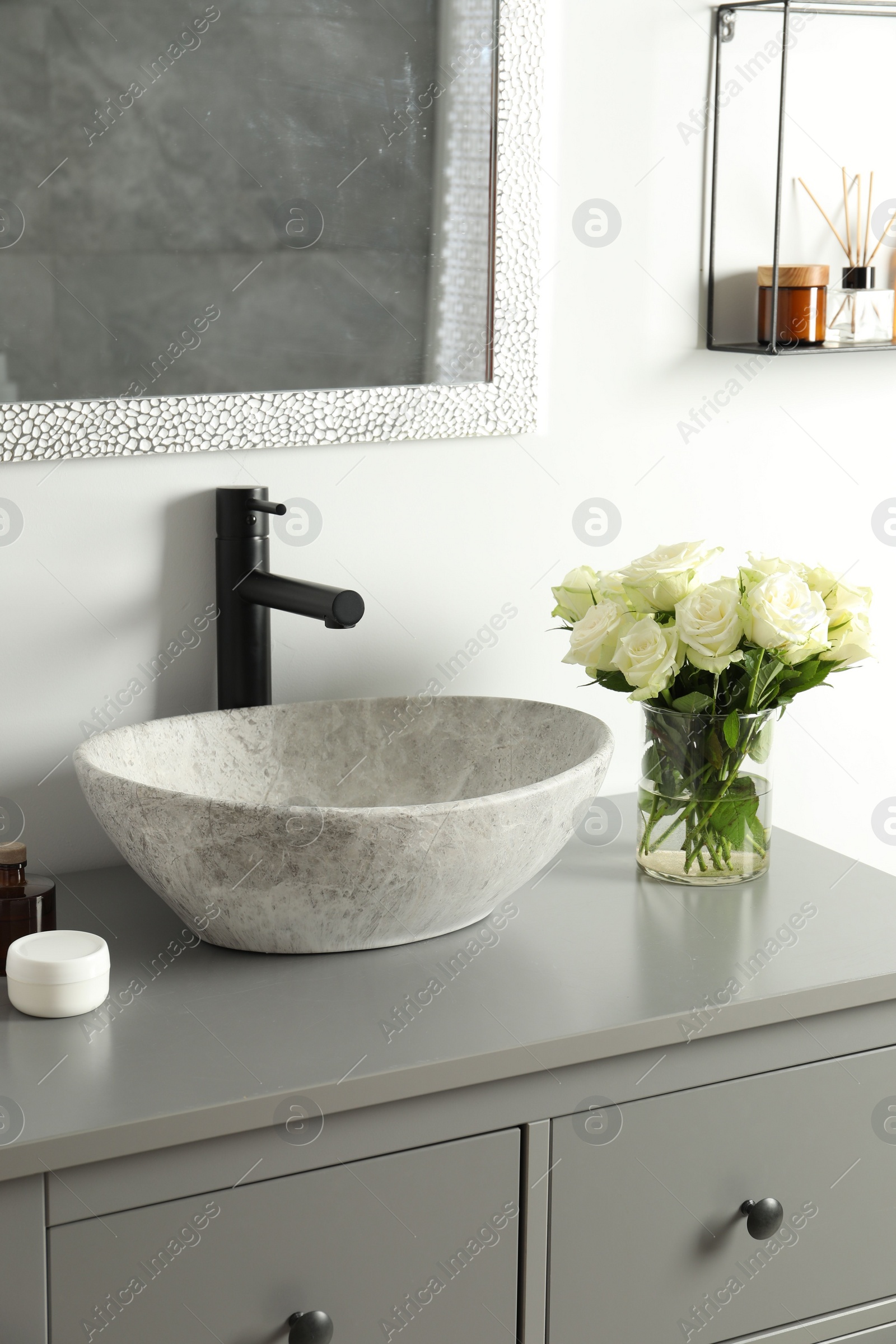 Photo of Vase with beautiful white roses and toiletries near sink in bathroom