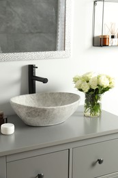 Vase with beautiful white roses and toiletries near sink in bathroom