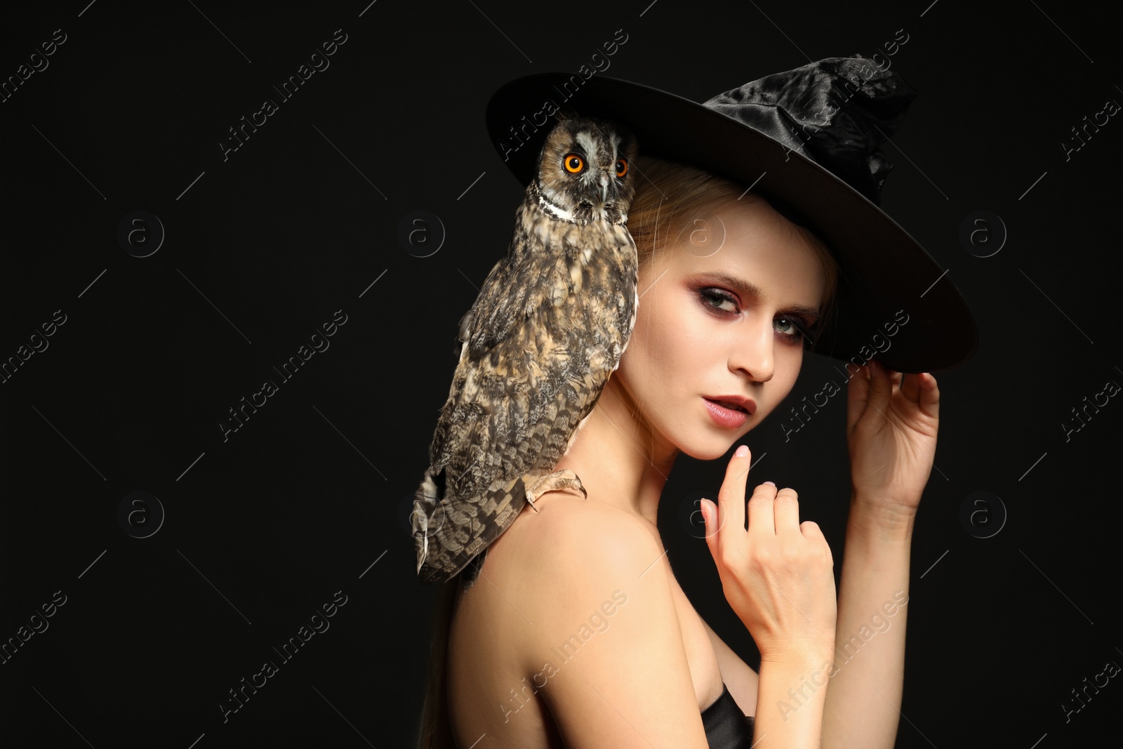 Photo of Witch in black hat with owl on dark background. Scary fantasy character