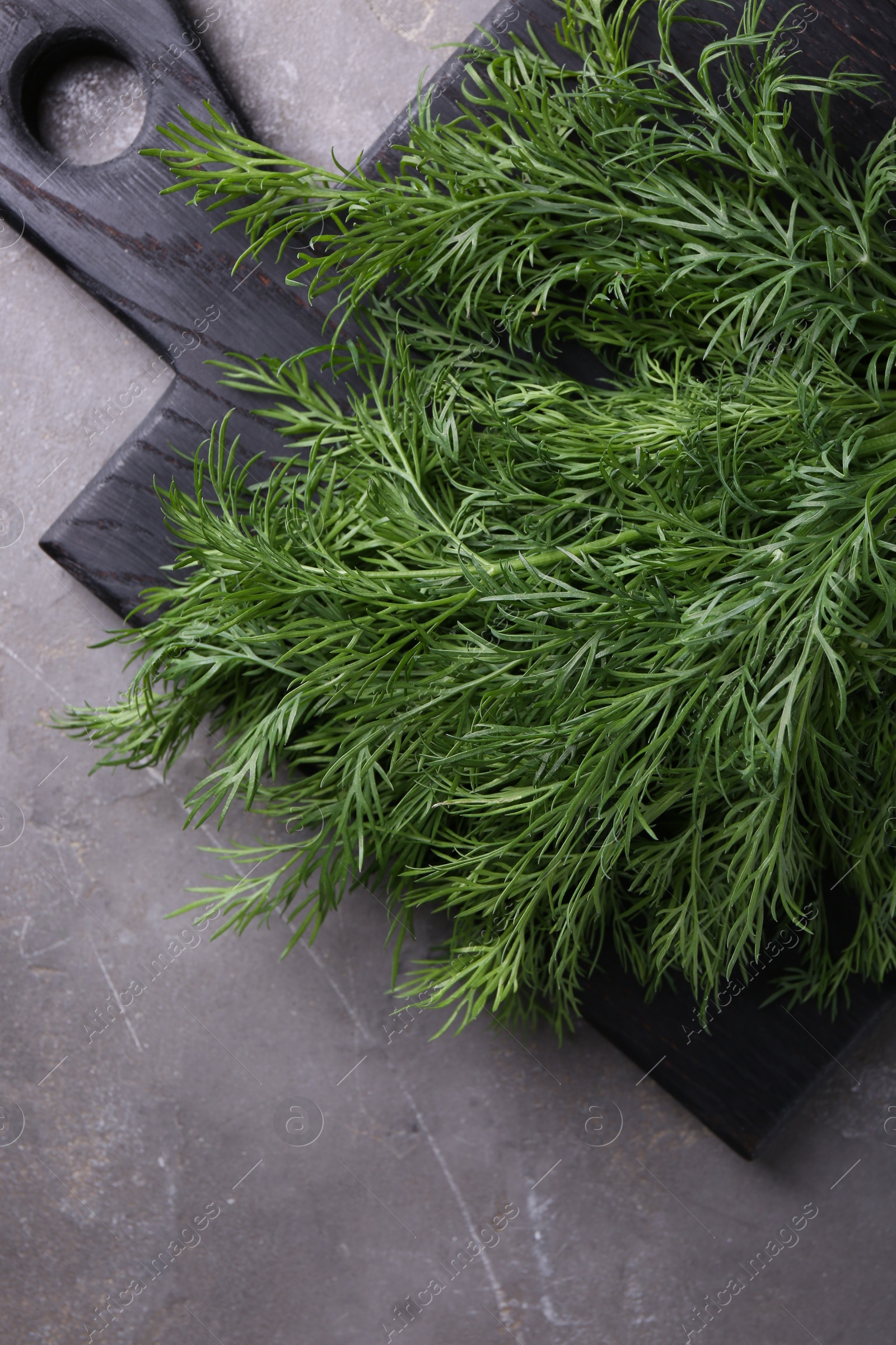 Photo of Board with sprigs of fresh dill on grey textured table, top view