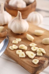 Photo of Aromatic cut garlic, cloves and bulbs on white wooden table, closeup