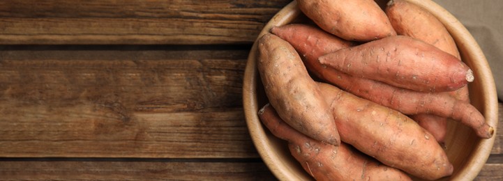 Fresh sweet potatoes in bowl on wooden table, top view with space for text. Banner design