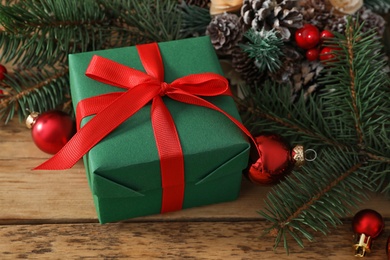 Photo of Green Christmas box with red bow and fir tree branches on wooden table