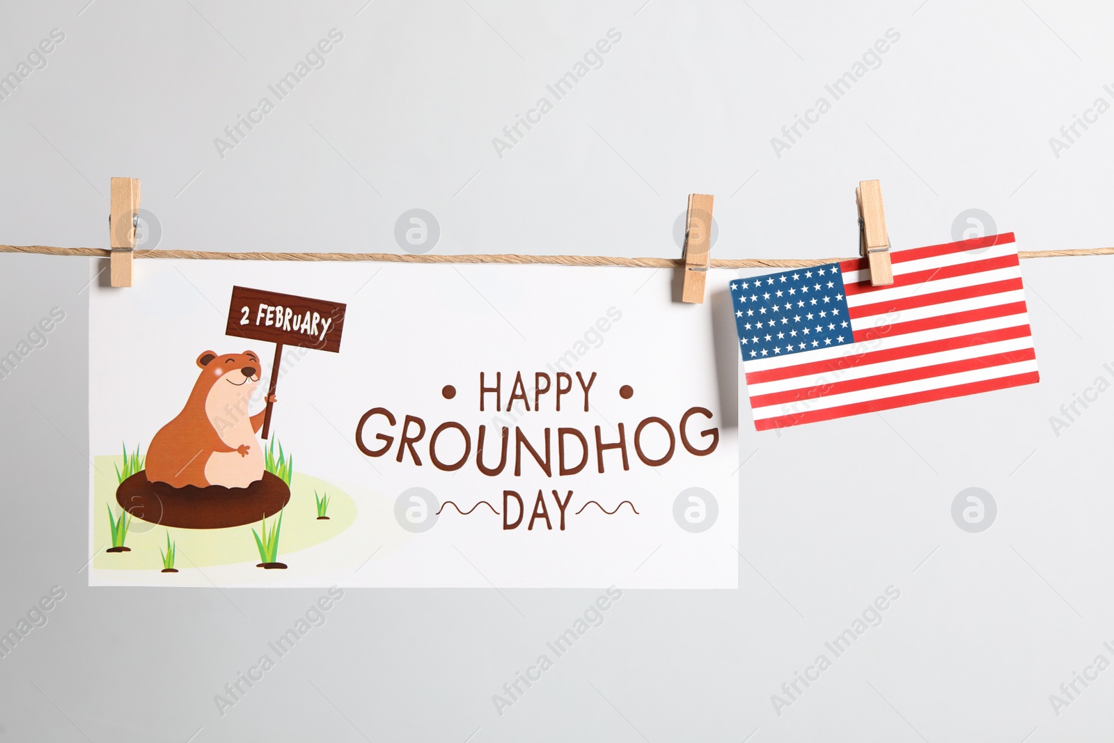 Photo of Happy Groundhog Day greeting card and American flag hanging on light background