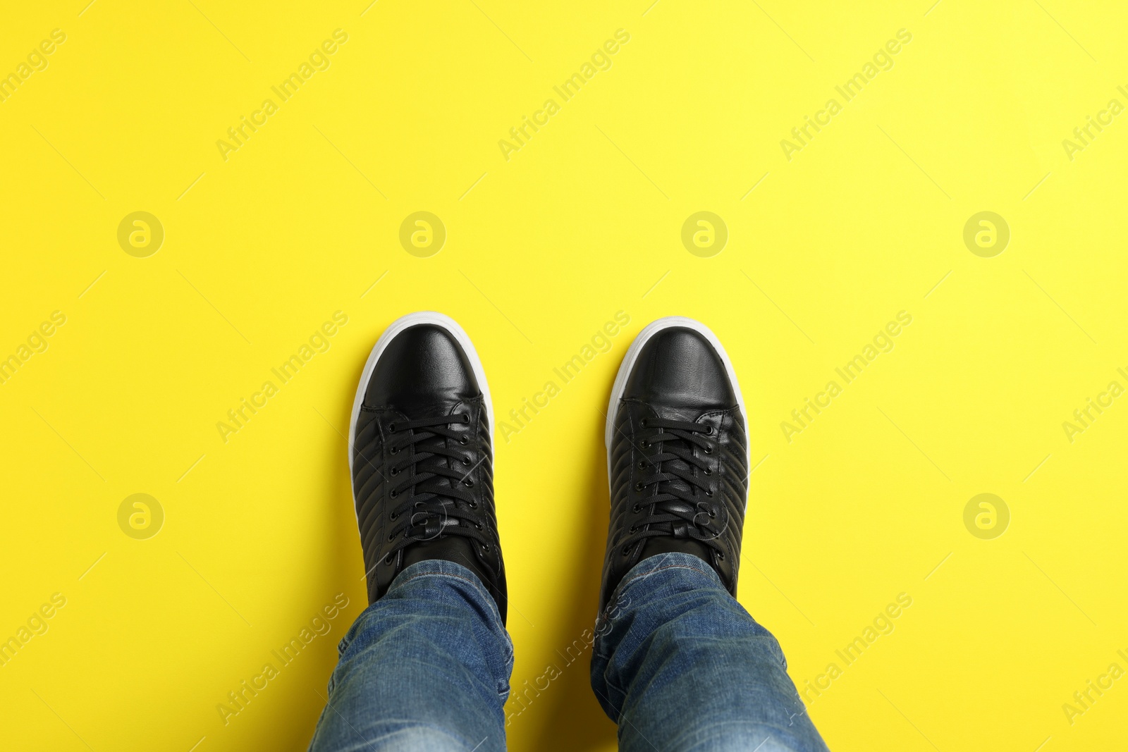 Photo of Man in stylish sneakers standing on yellow background, top view